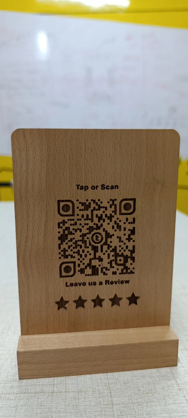Close-up of the Review+ beechwood standee showing high-density laser-engraved QR detail and engraved stars